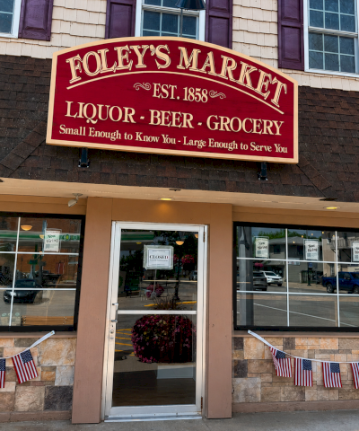 Foley&rsquo;s Market sign outside a store labeled liquor, beer, and grocery, with flags along the entrance.