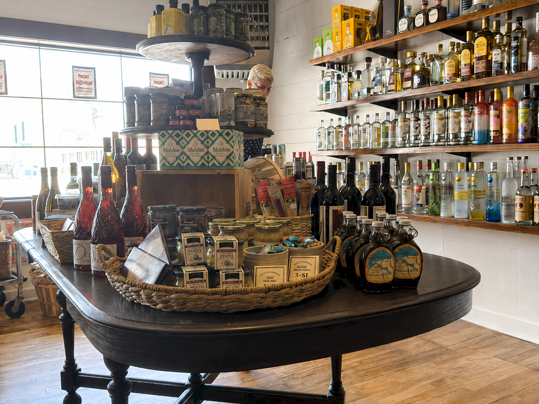 A cozy liquor shop with shelves of colorful bottles, a round serving table, and a staff member in the background, inside a store.